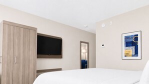 A hotel room with a bed, a wardrobe, a flat-screen TV mounted on the wall, a door leading to another room, and a framed abstract artwork on the wall. - Holiday Inn Express Dryden by IHG (Dryden)
