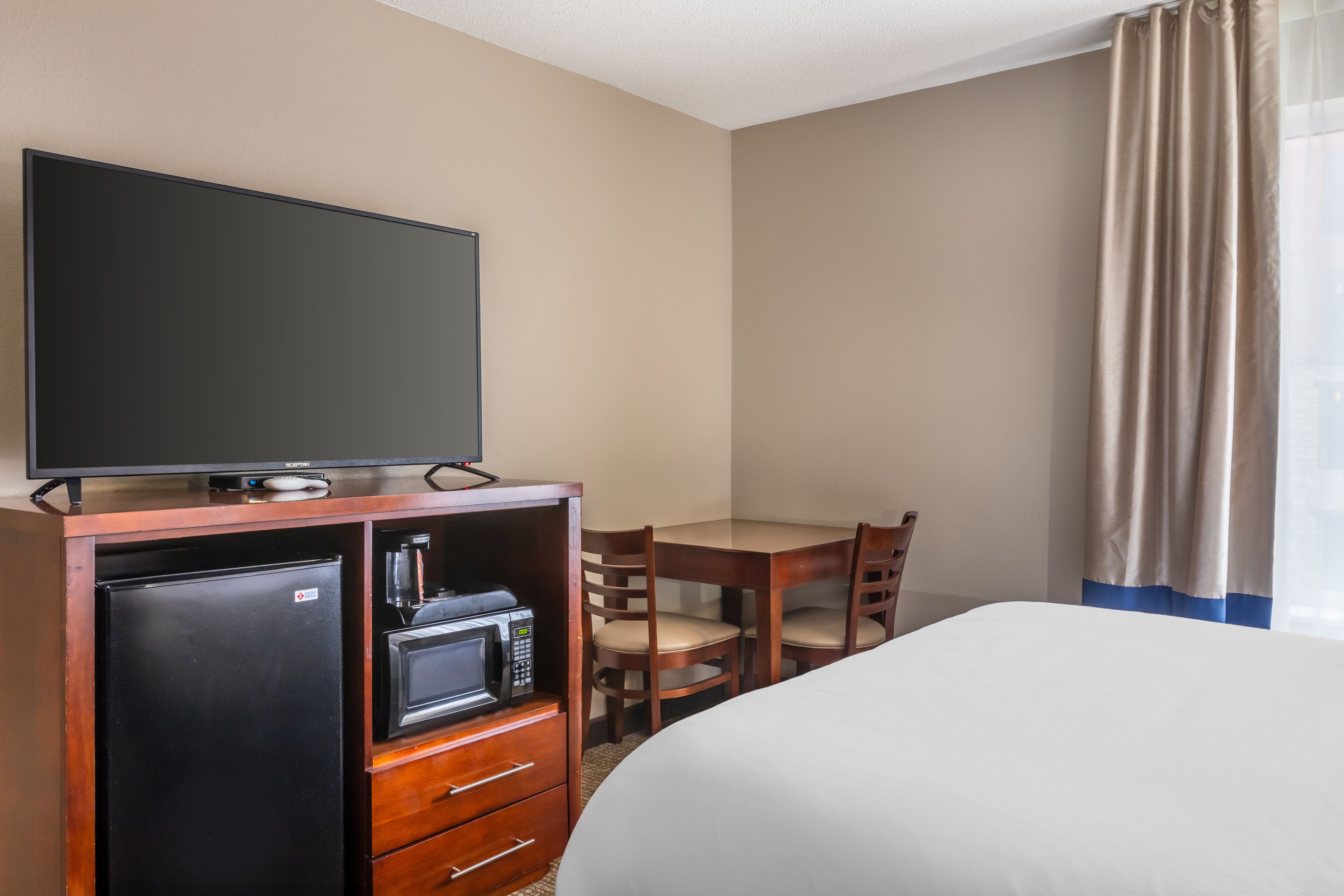 A hotel room with a bed, a desk with a chair, a television, a refrigerator, and a microwave.