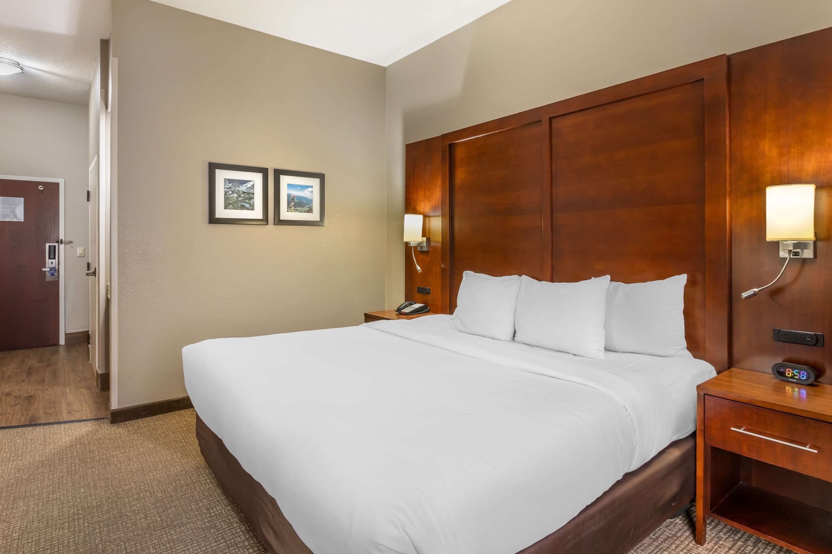 A hotel room with a large bed, a wooden headboard, two bedside tables with lamps, and a door to the left.