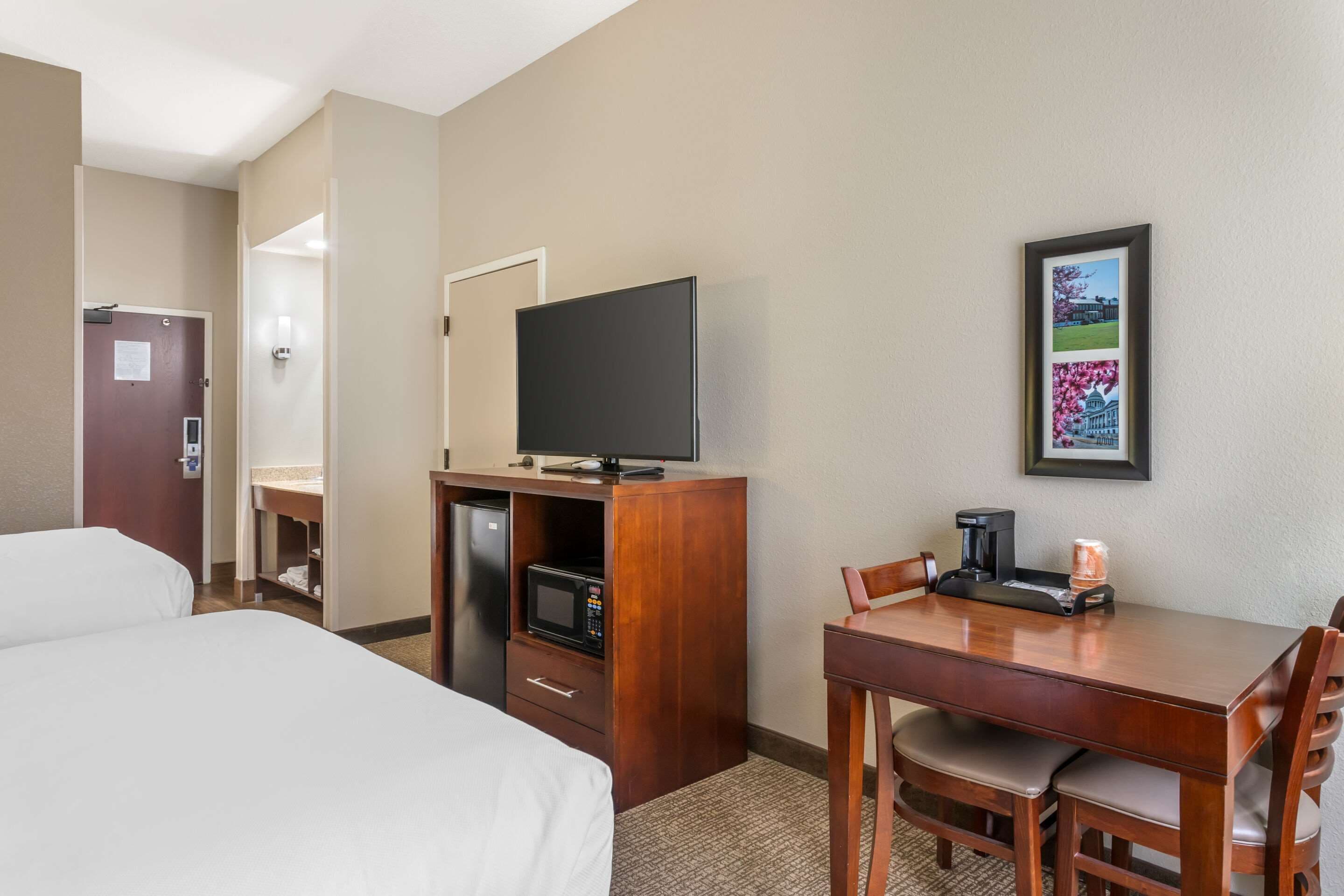 A hotel room with a bed, a desk with a chair, a television, a microwave, and a coffee maker.