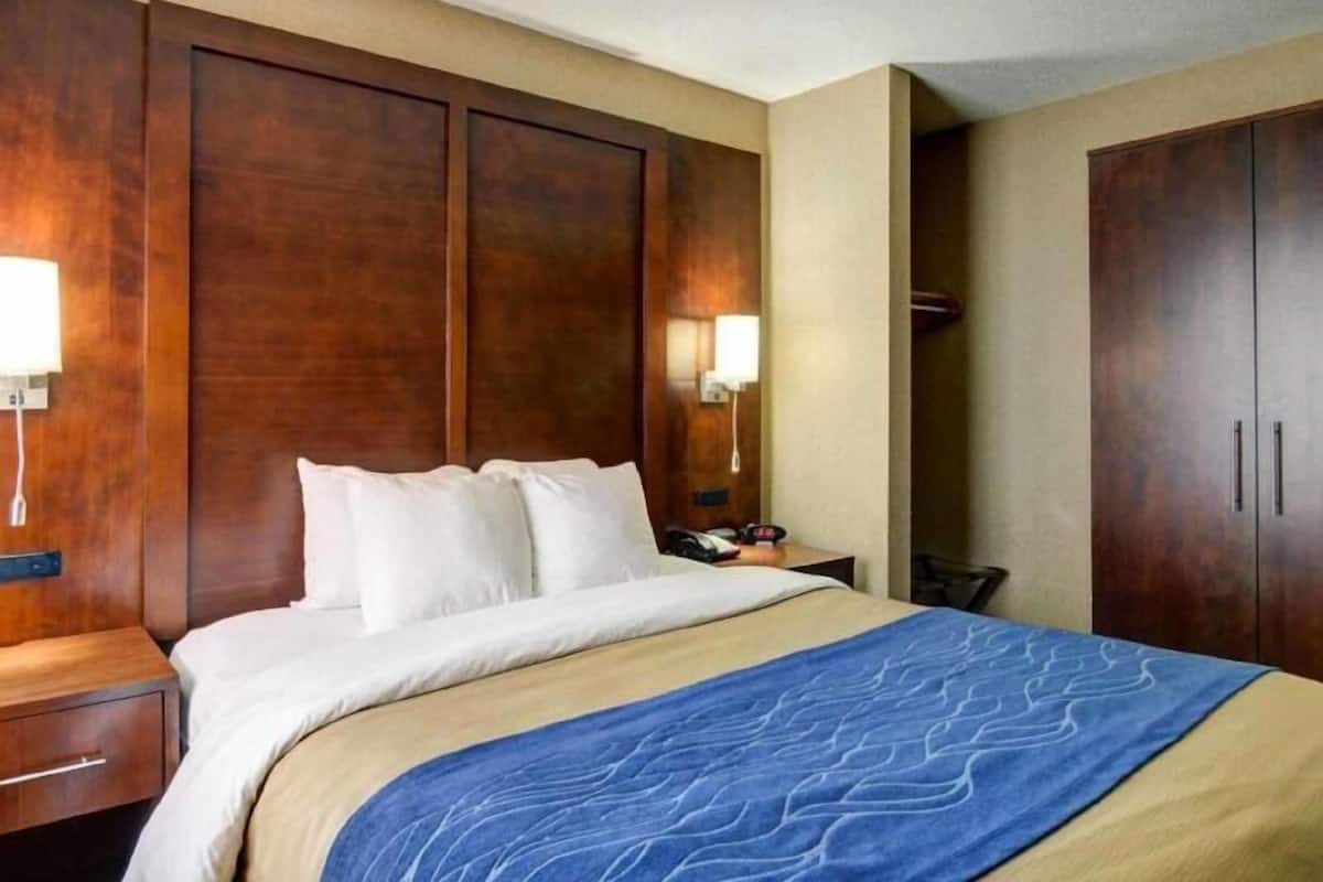 Una habitación de hotel con cama, mesitas de noche, armario y lámparas fijadas a la pared.