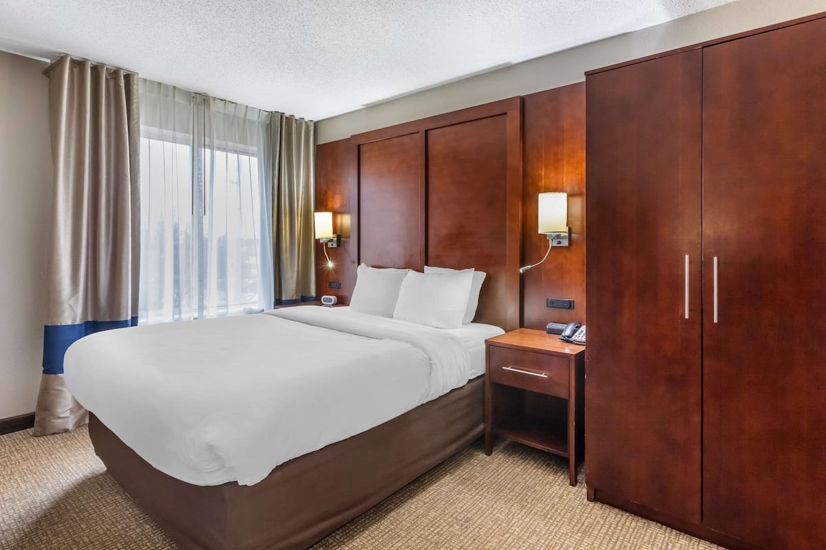 Habitación de hotel con una cama grande, armario de madera, lámparas de noche y vistas de la ciudad a través del ventanal.