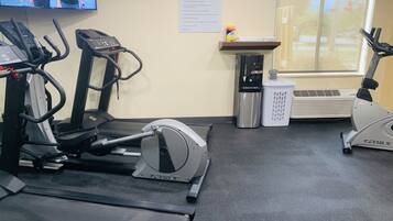 A fitness center with treadmills, an elliptical, a water dispenser, and a TV displaying a fitness program.