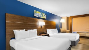 A hotel room with two beds, a wooden headboard, a wall-mounted lamp, and a large window.