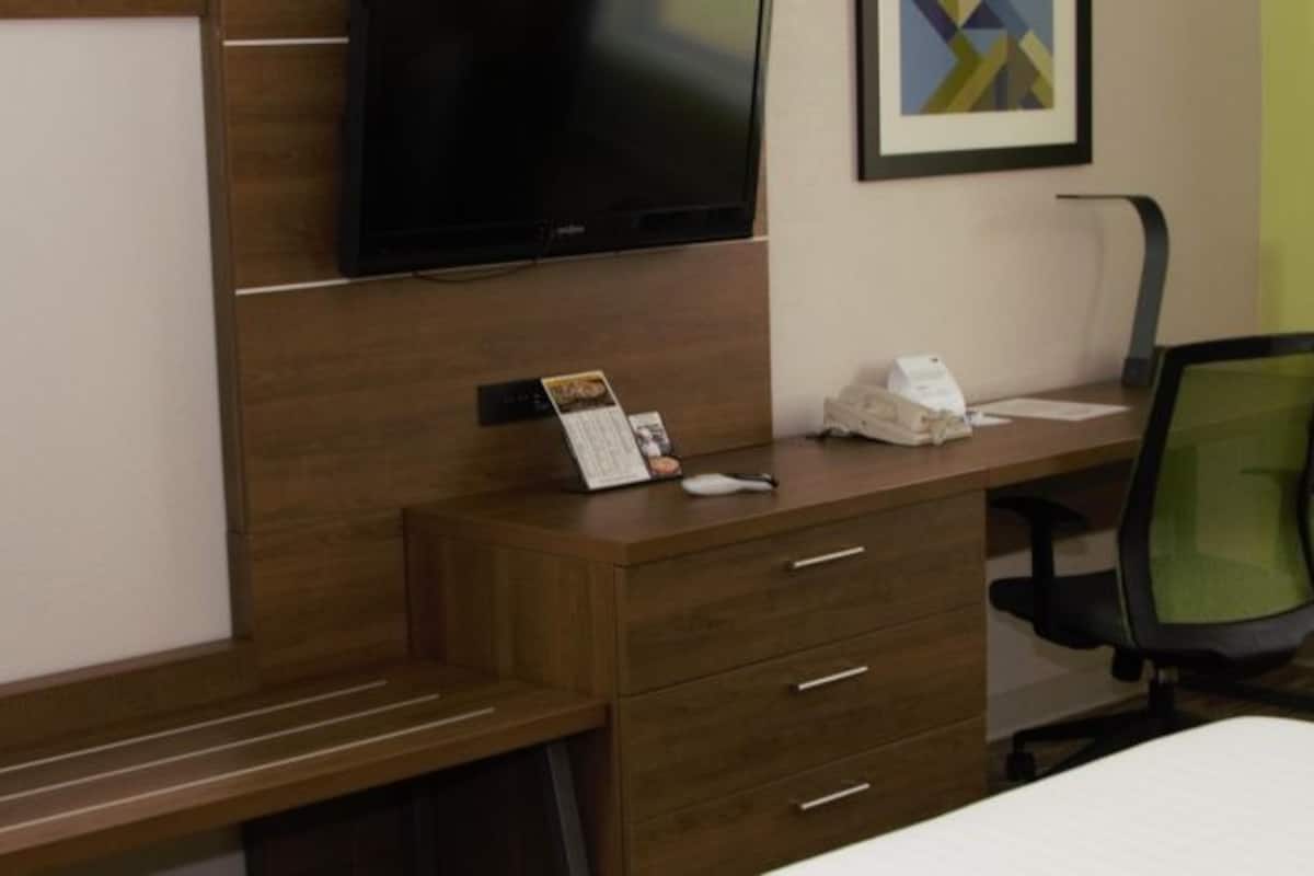A hotel room with a bed, a desk with a chair, a television, and a wardrobe.