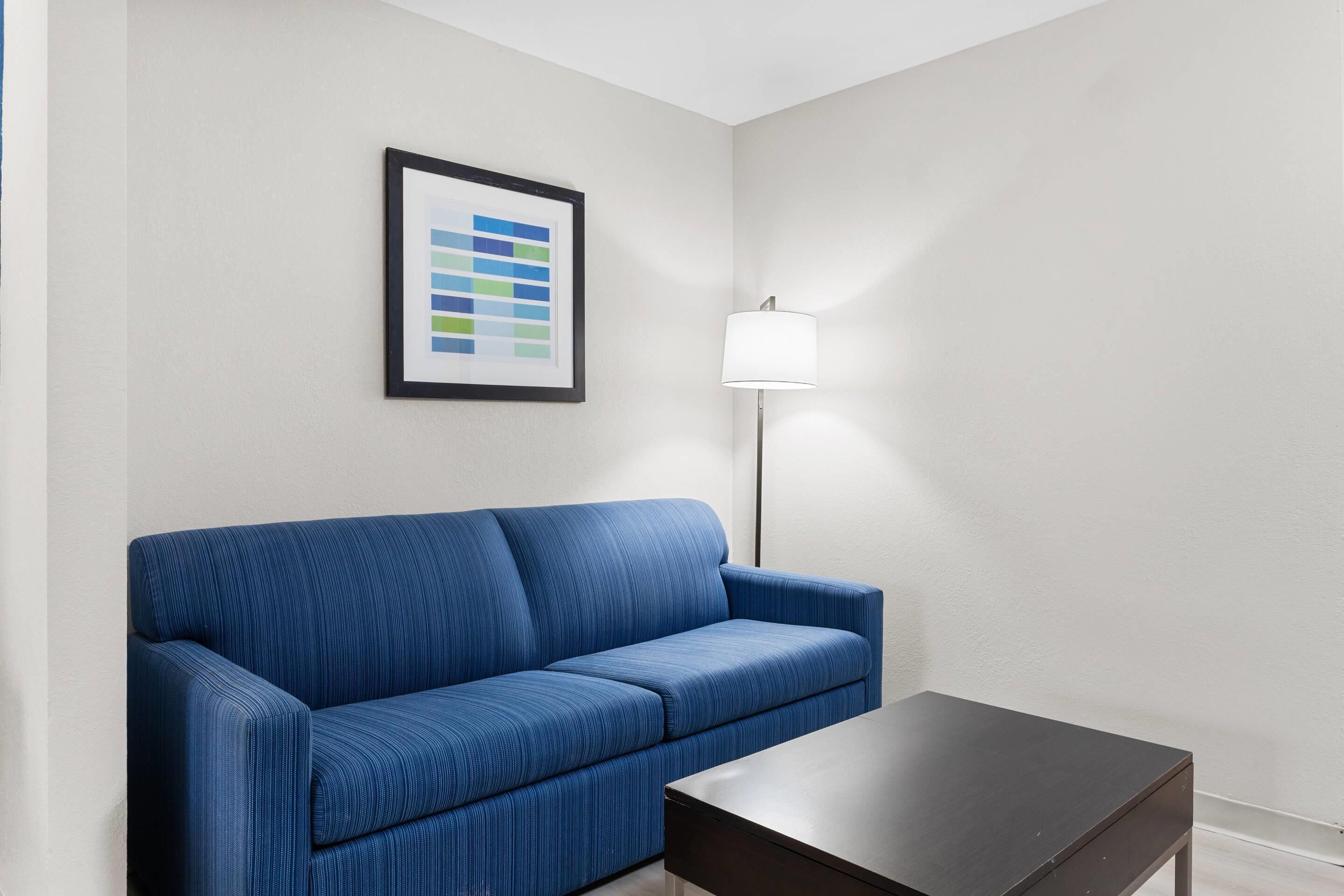 A room with a blue sofa, a small table, a floor lamp, and a framed color palette on the wall.