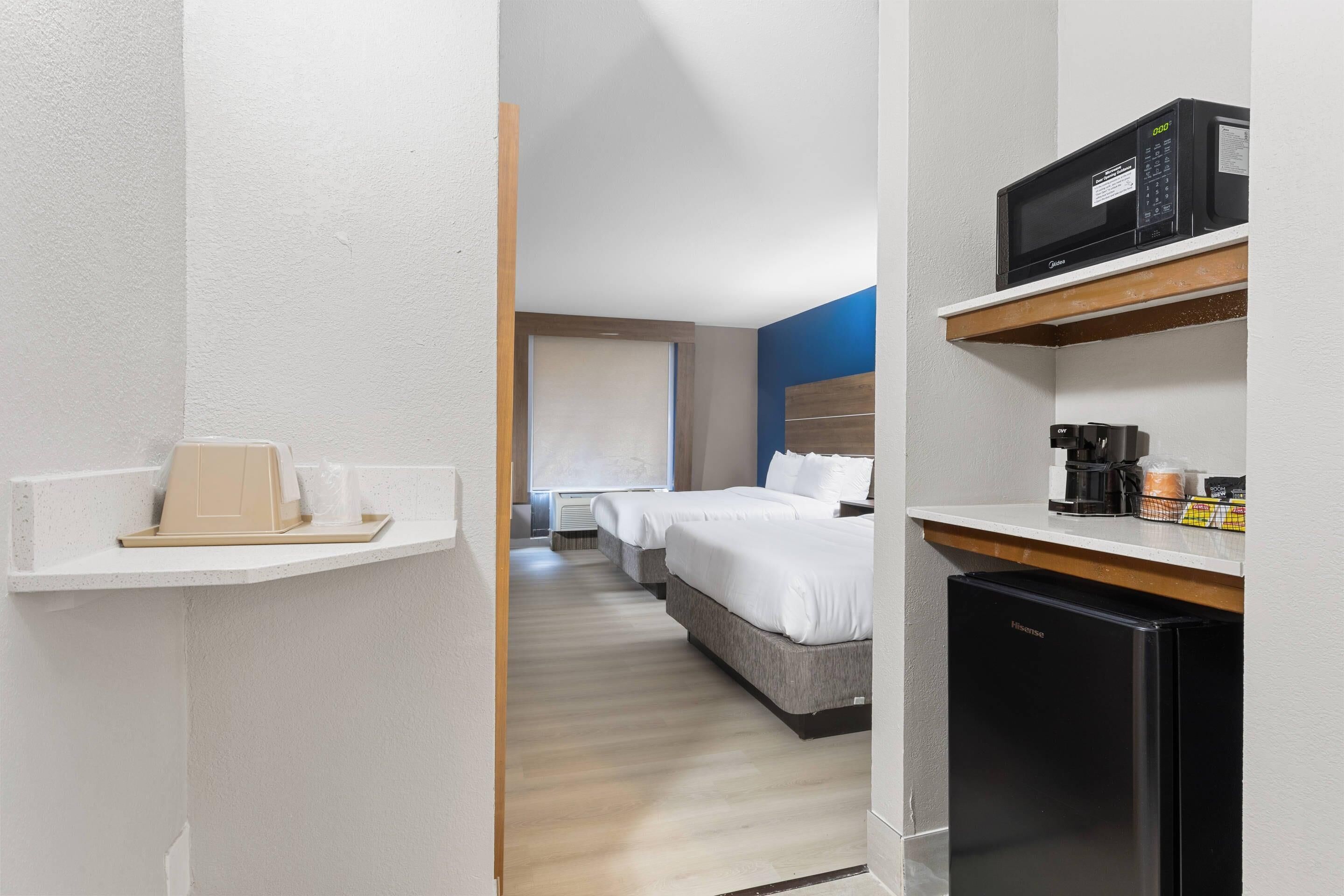 Una habitación de hotel con una cama, microondas, refrigerador y una pequeña zona de kitchenette.
