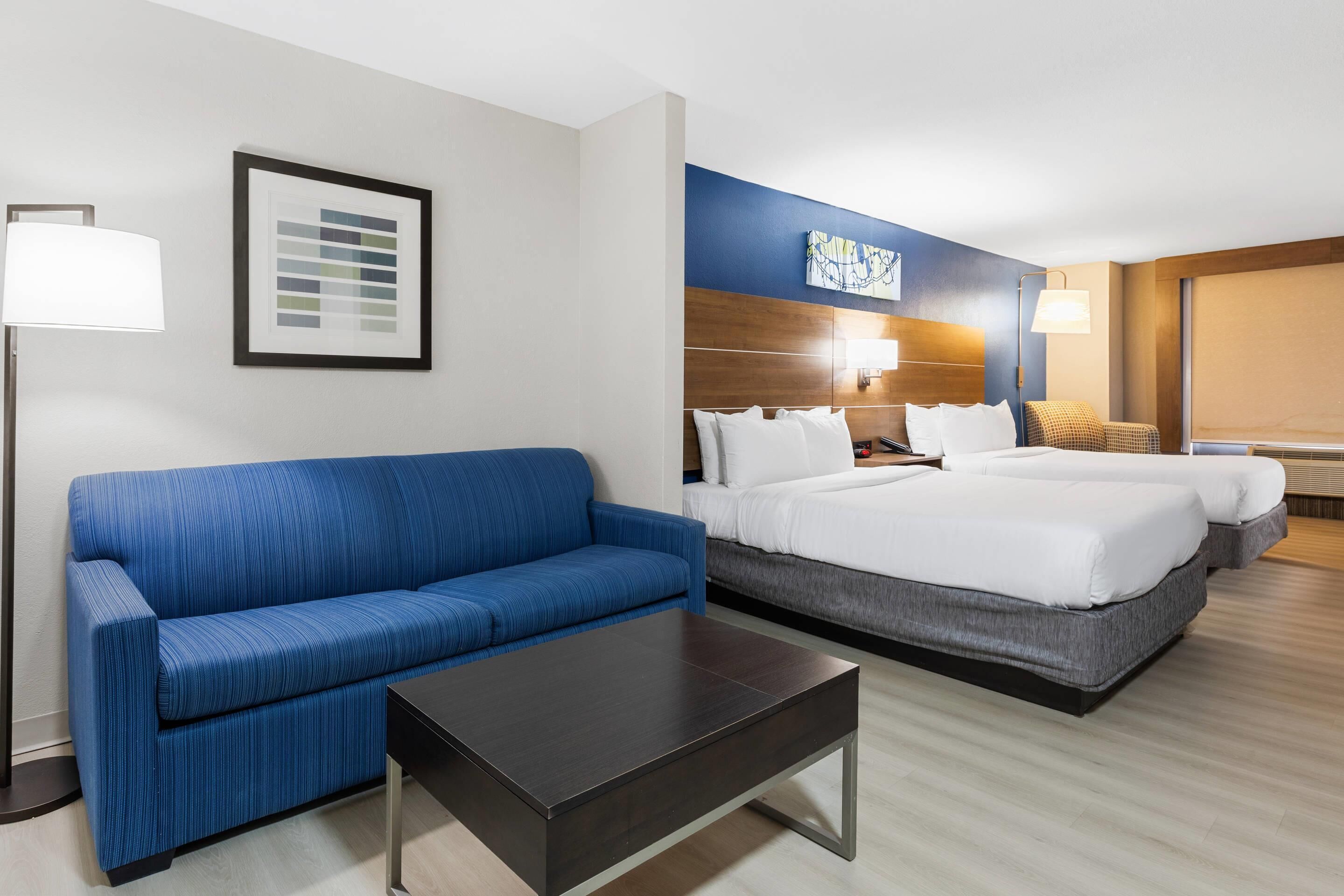 A hotel room with a blue sofa, a bed with white bedding, a dark wooden coffee table, and a framed picture on the wall.