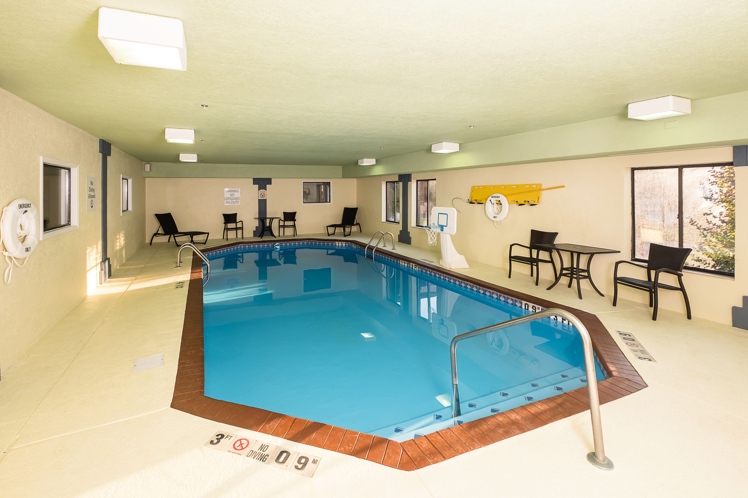 An indoor swimming pool with a tiled floor, a lifeguard chair, and a yellow lifeguard stand.