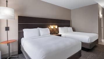 A hotel room with two beds, a nightstand, a lamp, and a wall-mounted light.