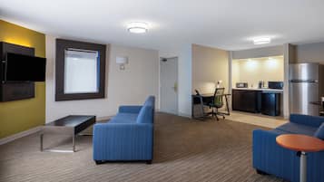 Une chambre d’hôtel moderne équipée d’un téléviseur à écran plat, d’un canapé, d’une petite table, d’un bureau, d’une chaise et d’une kitchenette.