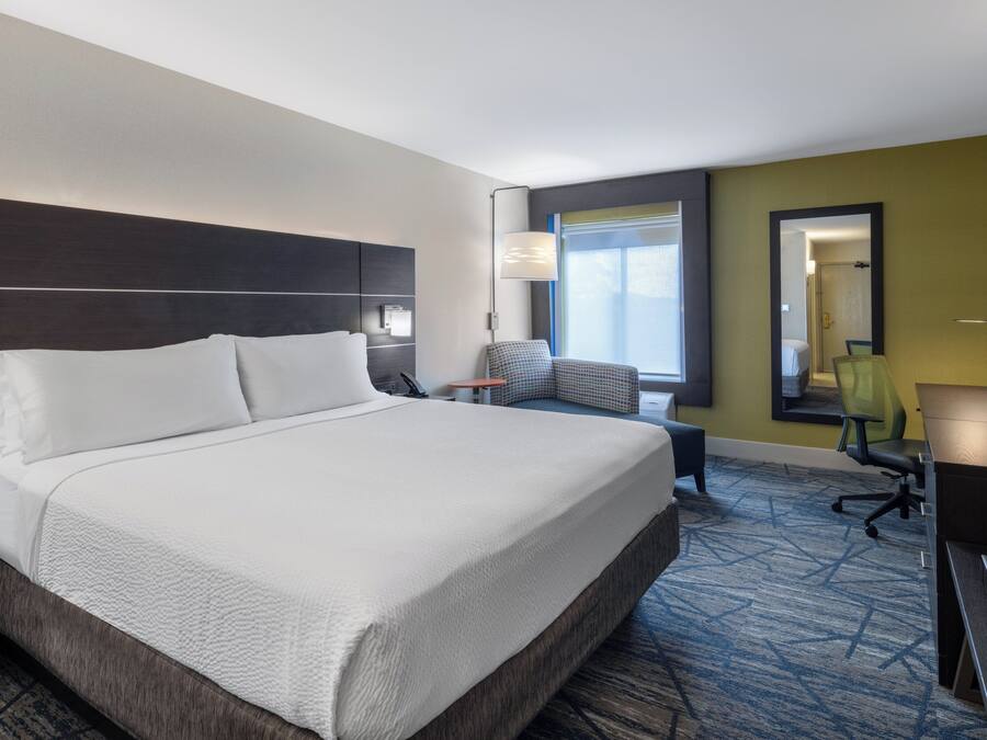A hotel room with a large bed, a desk, a chair, a small table, a lamp, and a window with a view.