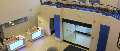 A hotel lobby with a reception desk, seating area, and a staircase leading to an upper level.