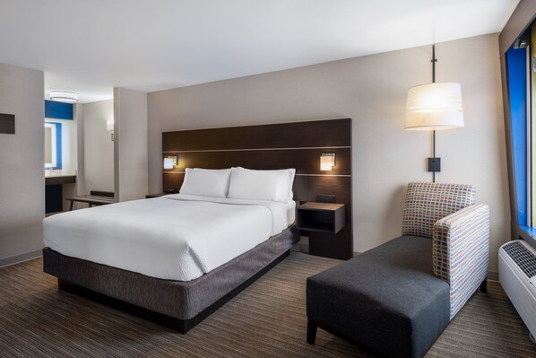 A modern hotel room with a large bed, a bedside table, a chair, and a wall-mounted lamp. - Holiday Inn Express Corydon by IHG (Corydon)