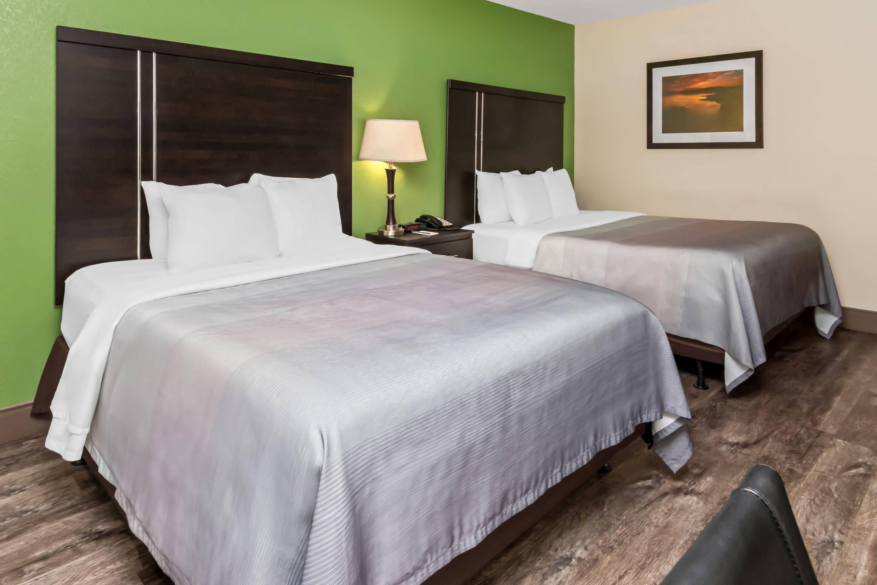 A hotel room with two beds, a nightstand with a lamp, and a framed picture on the wall.