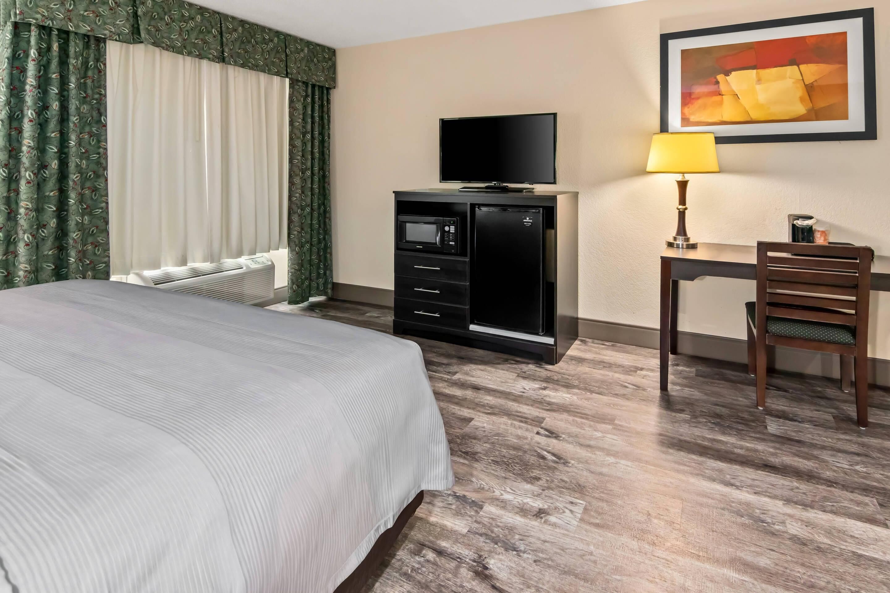 Une chambre d’hôtel équipée d’un lit, d’un bureau avec une lampe, d’une télévision et d’un four à micro-ondes.