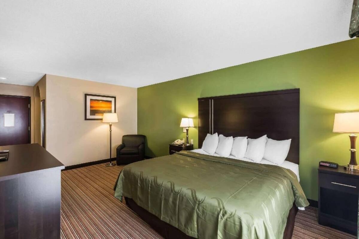 Habitación de hotel con cama, escritorio, silla, dos mesitas de noche con lámparas y un cuadro en la pared.