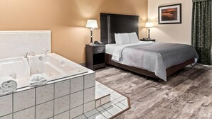 Quarto de hotel com uma banheira grande, uma cama com cabeceira, mesa de cabeceira com abajur e um quadro na parede.