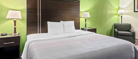 Una habitación de hotel con una cama grande, dos mesitas de noche con lámparas, una silla y paredes verdes.