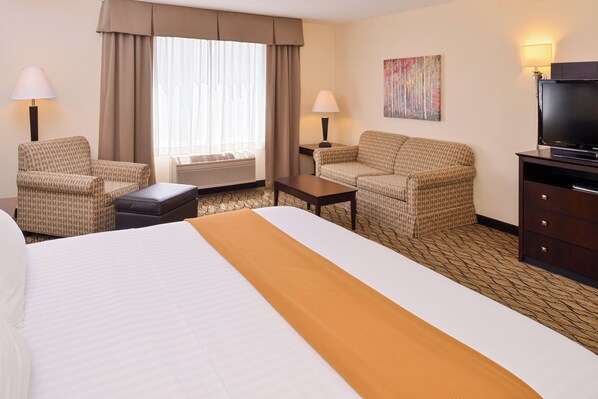 A hotel room with a bed, two armchairs, a small table, a sofa, a TV, and a painting on the wall.