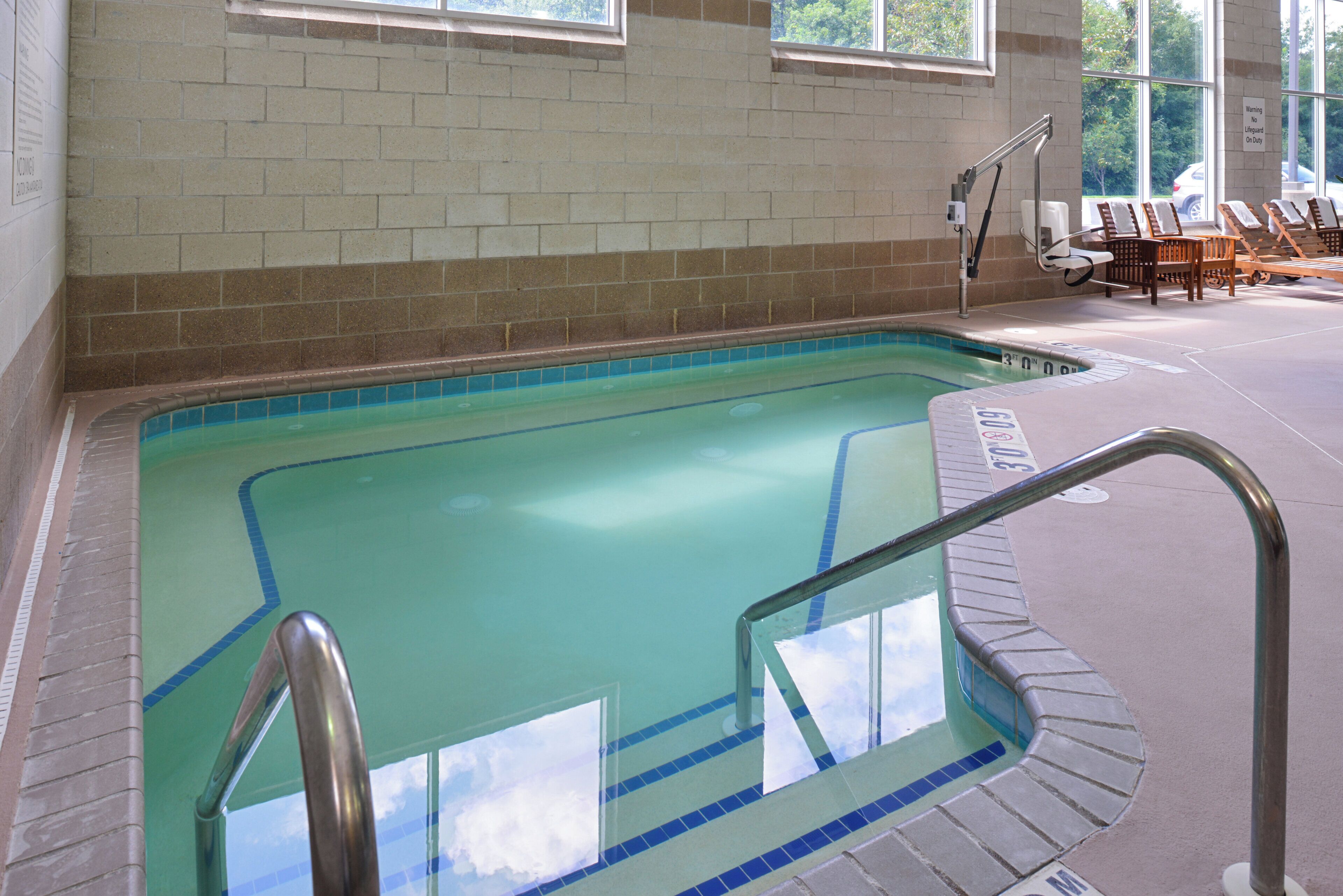 An indoor swimming pool with clear water, a lifeguard chair, and lounge chairs.