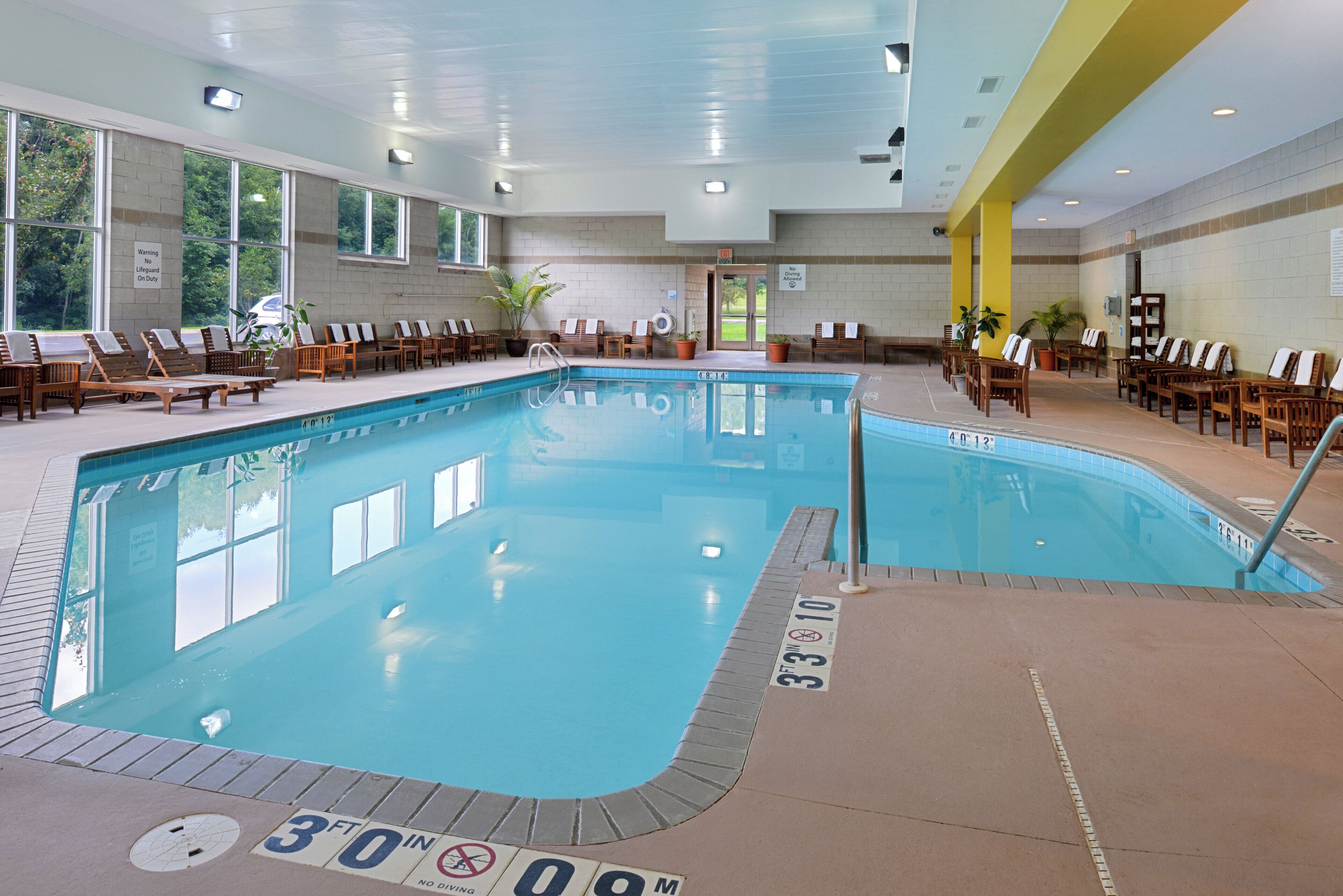 An indoor swimming pool with clear water, marked depth lines, and lounge chairs around the perimeter.