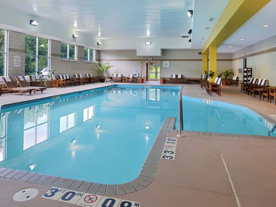 En indendørs swimmingpool med klart vand, dybdemarkeringer og liggestole hele vejen rundt.