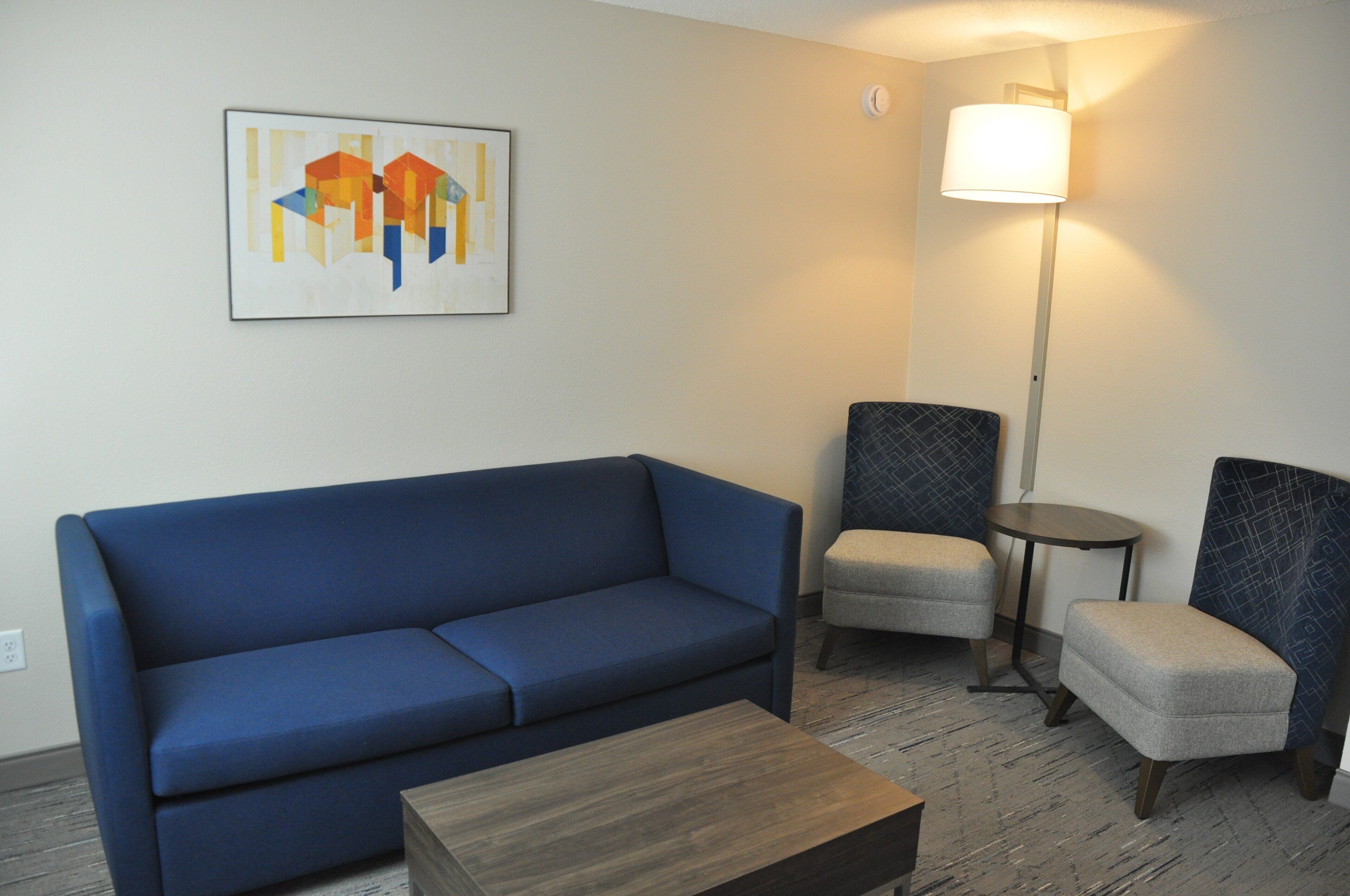 A room with a blue sofa, two armchairs, a small table, and a floor lamp.