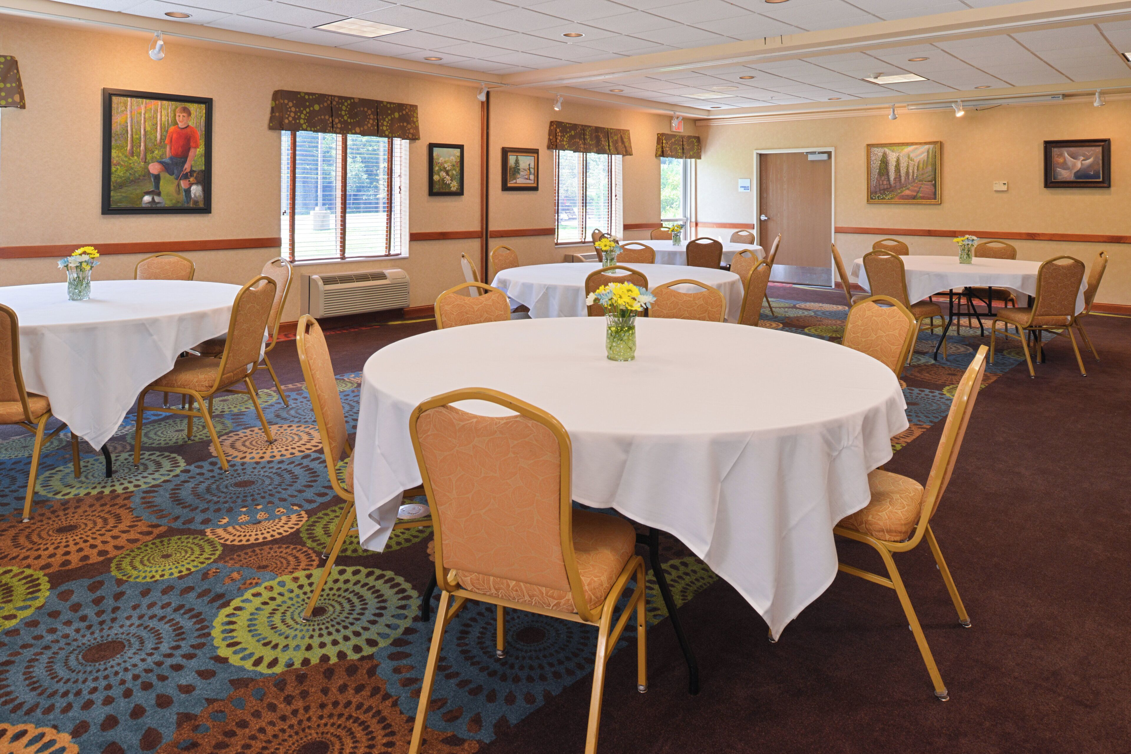 Une salle de conférence d’hôtel avec des tables rondes, des chaises et des centres de table floraux.