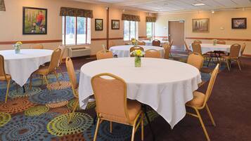 Une salle de conférence d’hôtel avec des tables rondes, des chaises et des centres de table floraux.