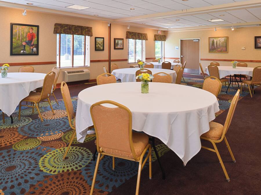 Une salle de conférence d’hôtel avec des tables rondes, des chaises et des centres de table floraux.