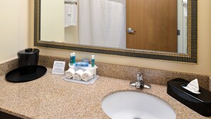 A hotel bathroom with a granite countertop, a white sink, a mirror with a decorative frame, a towel rack, and a hand dryer.