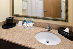 A hotel bathroom with a granite countertop, a white sink, a mirror with a decorative frame, a towel rack, and a hand dryer.