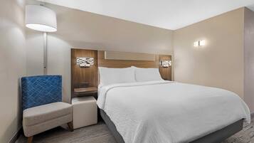 A hotel room with a bed, a chair, a nightstand, a lamp, and a wall-mounted light fixture.