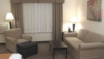 A hotel room with two sofas, a small table, and a window with curtains.