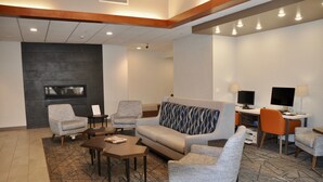 A modern lobby with a sofa, armchairs, a coffee table, a flat-screen TV, and a desk with a computer.