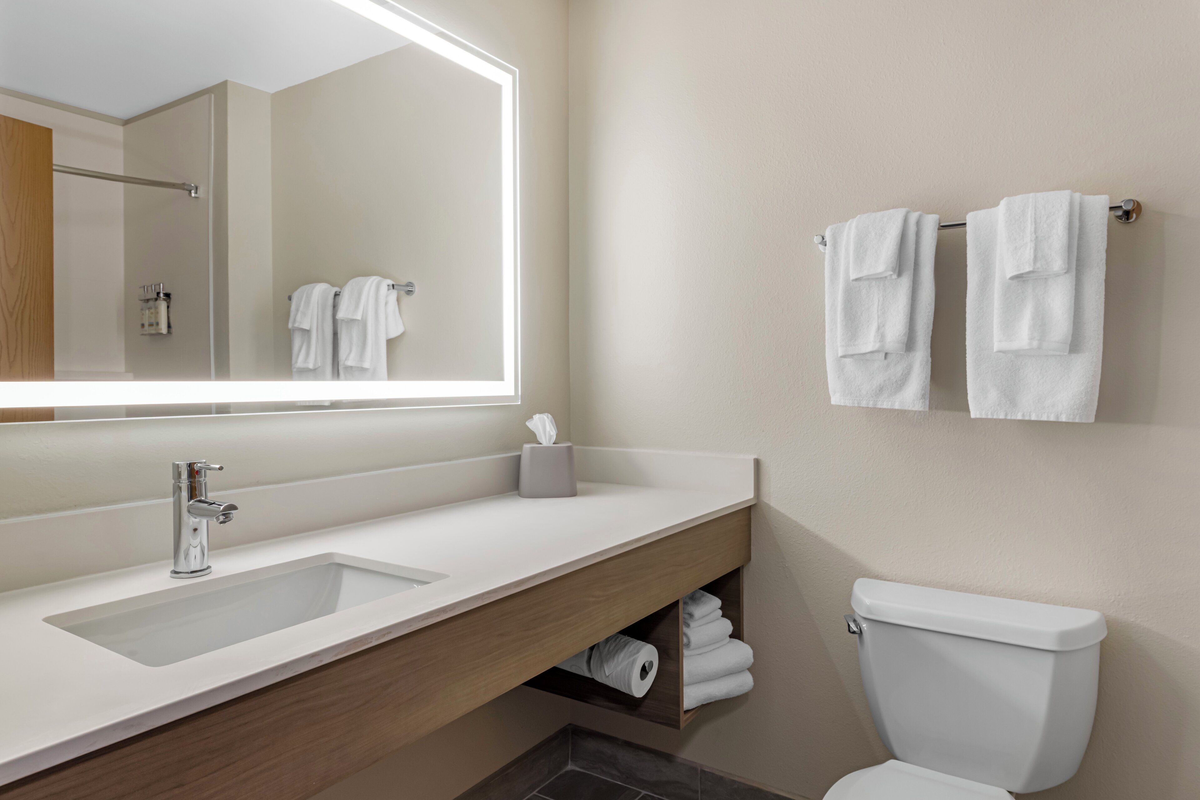 A modern bathroom with a large mirror, a sink, a toilet, and a towel rack.