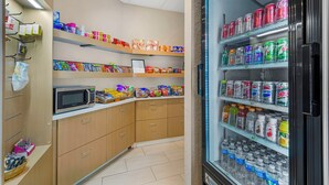A kitchenette with a microwave, shelves stocked with snacks, and a refrigerator with beverages.