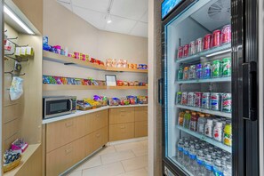 A kitchenette with a microwave, shelves stocked with snacks, and a refrigerator with beverages.