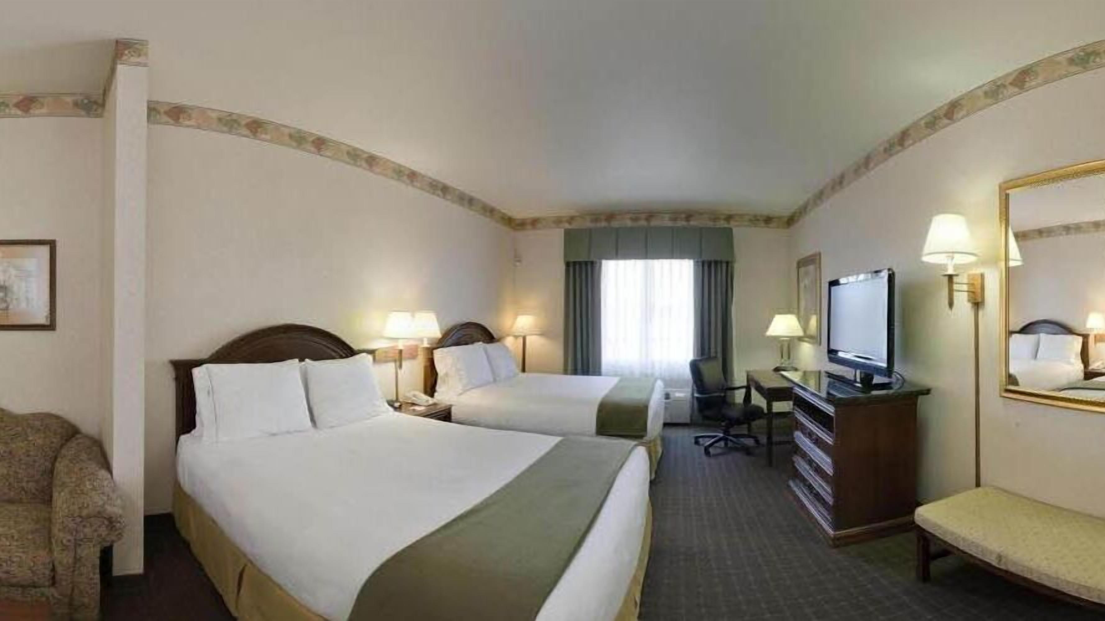 A hotel room with two beds, a desk, a chair, a television, and a mirror.