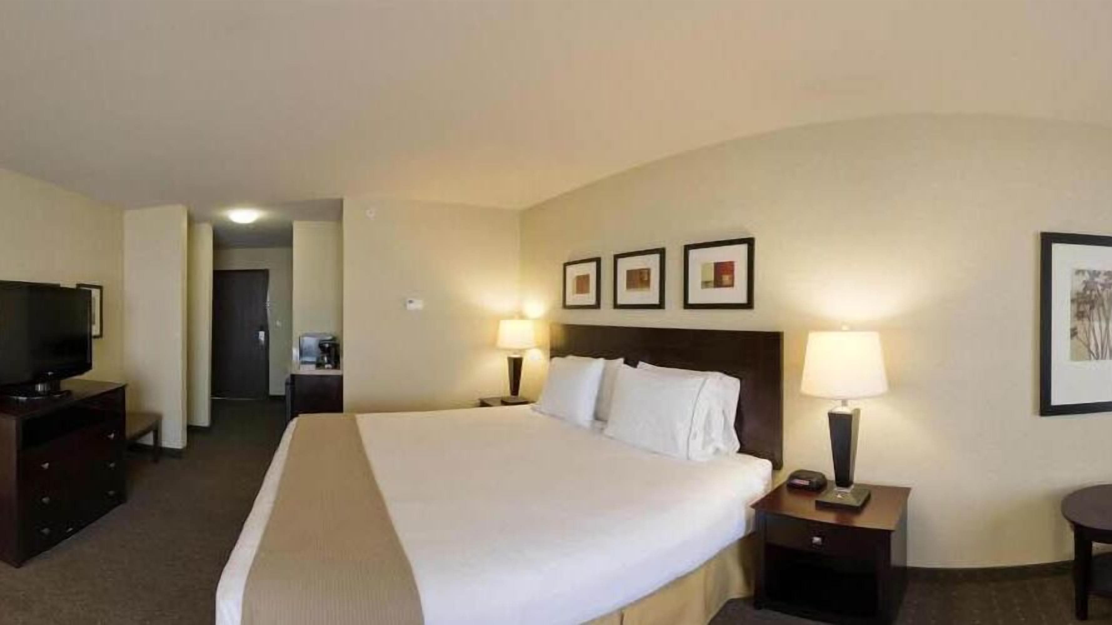 A hotel room with a large bed, two bedside tables with lamps, a TV, and framed pictures on the wall.