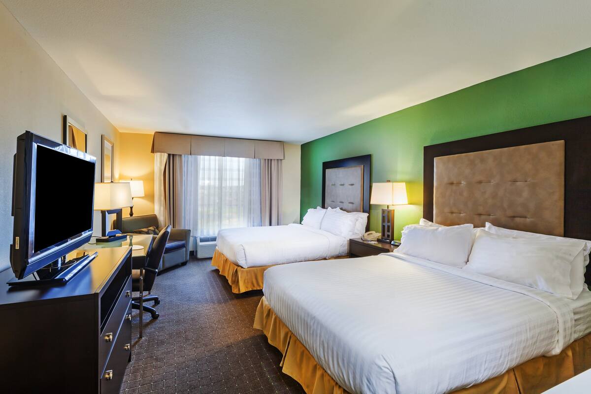 A hotel room with two beds, a desk with a computer, a TV, and a window with curtains.