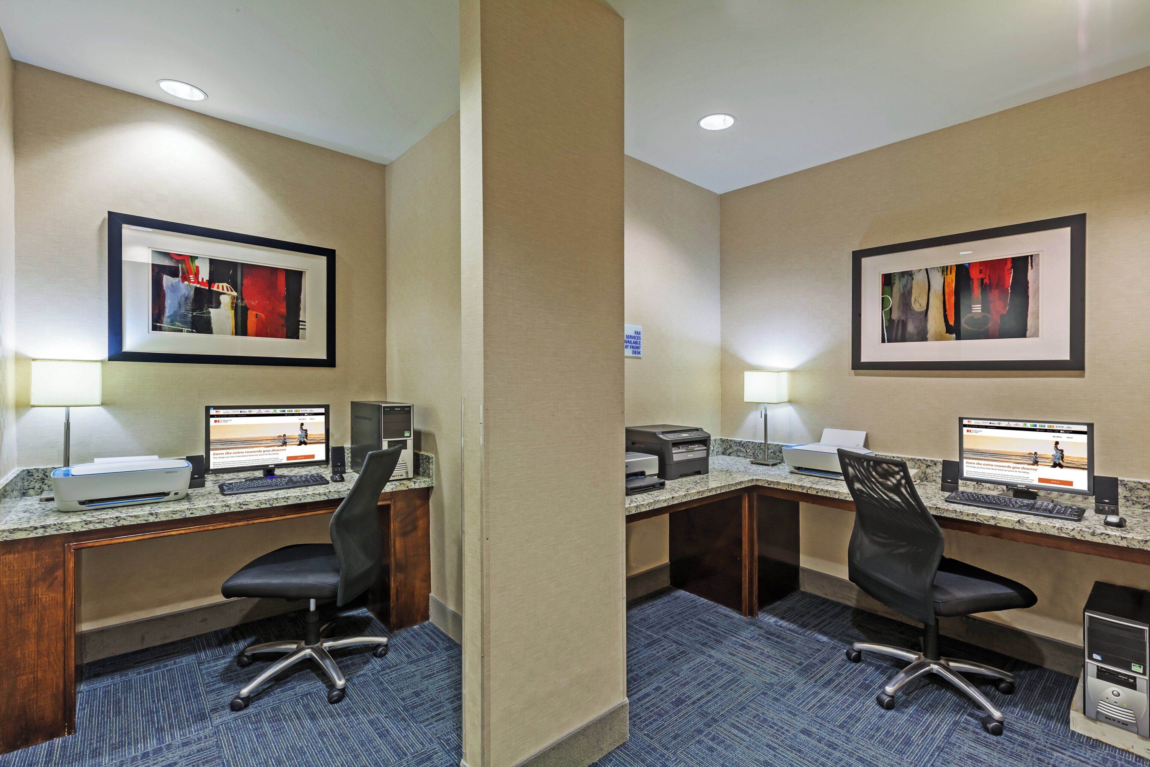 Habitación de hotel con dos escritorios, cada uno equipado con una computadora, impresora y lámpara de escritorio.