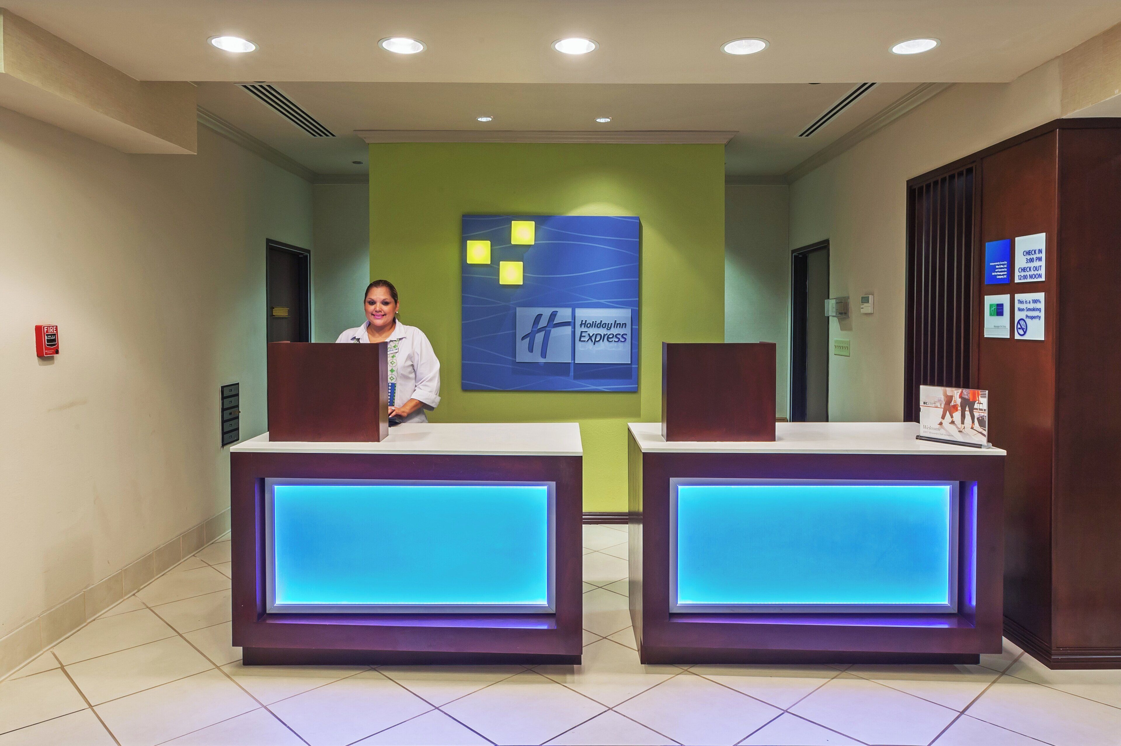 Una recepción de hotel con una recepcionista, un letrero de Holiday Inn Express y un horario de registro de entrada y salida.