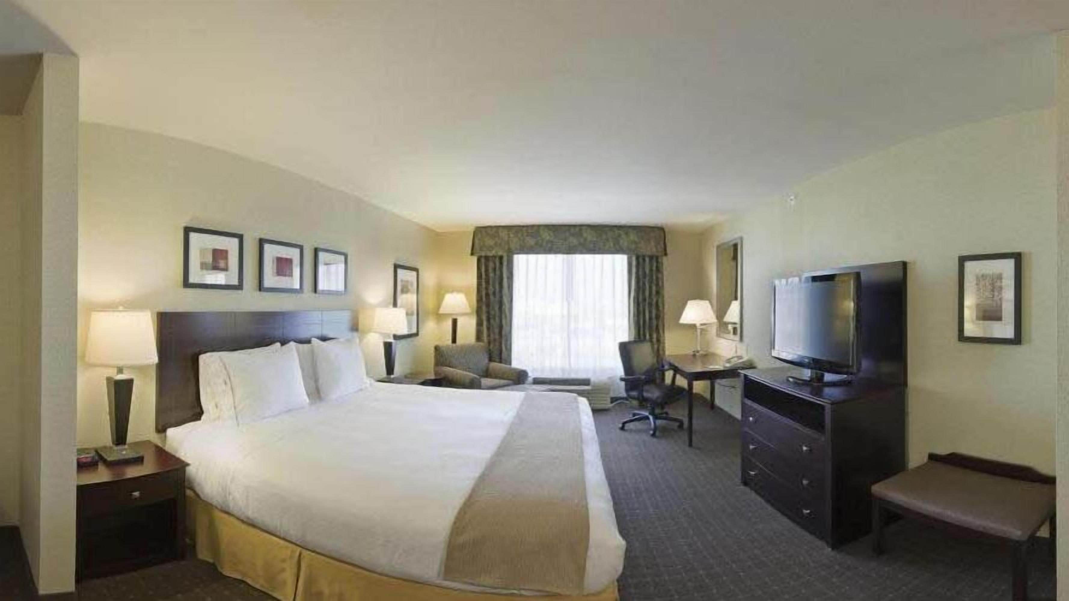 Quarto de hotel com uma cama grande, uma escrivaninha, uma televisão e uma cadeira.