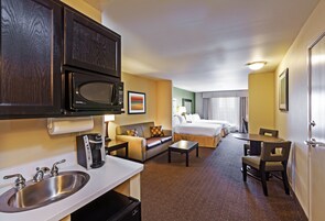 Habitación de hotel con kitchenette, una cama, un sofá, una mesa de comedor y un baño pequeño.