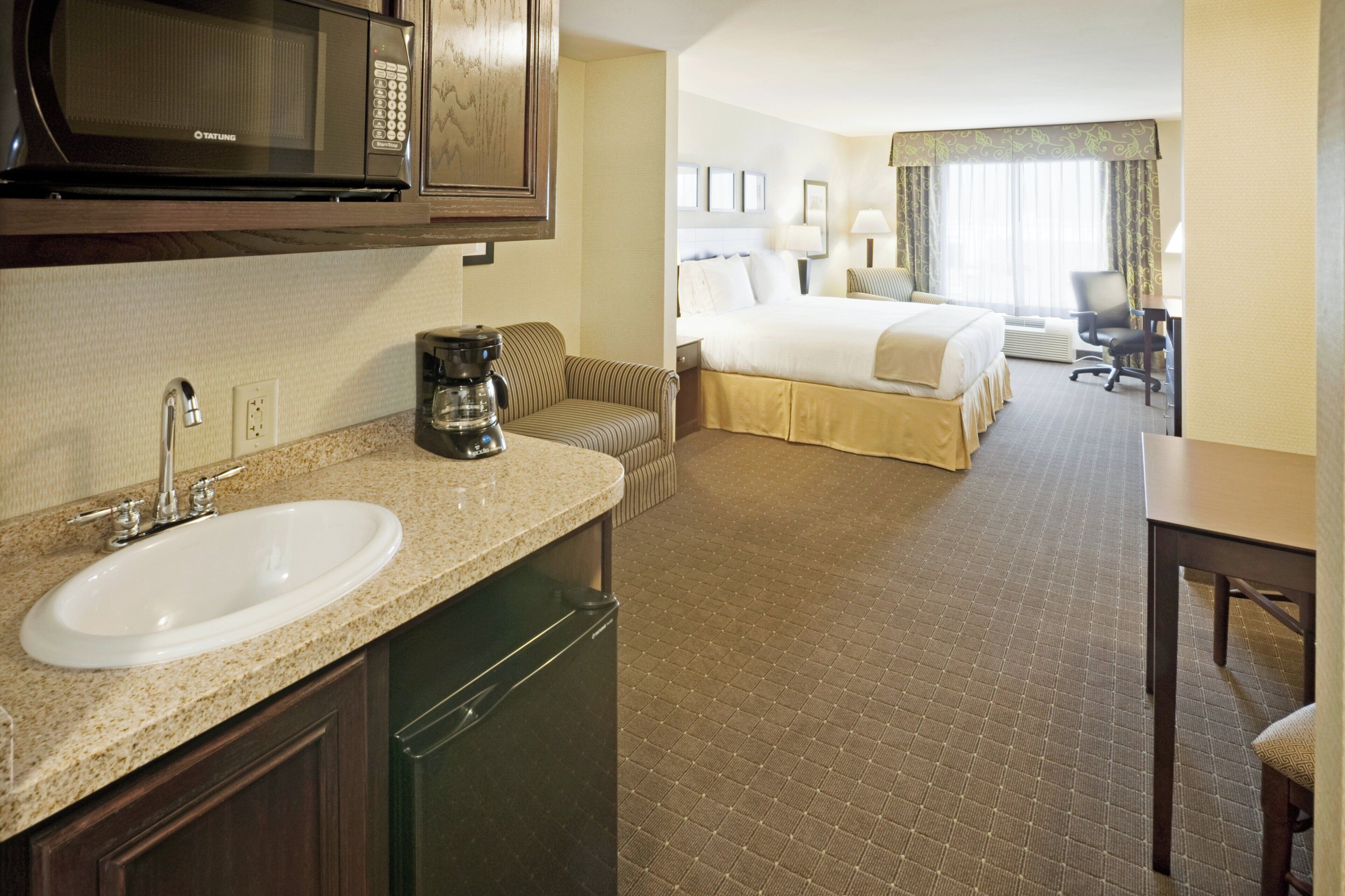 A hotel room with a kitchenette, a bed, a desk, and a bathroom.