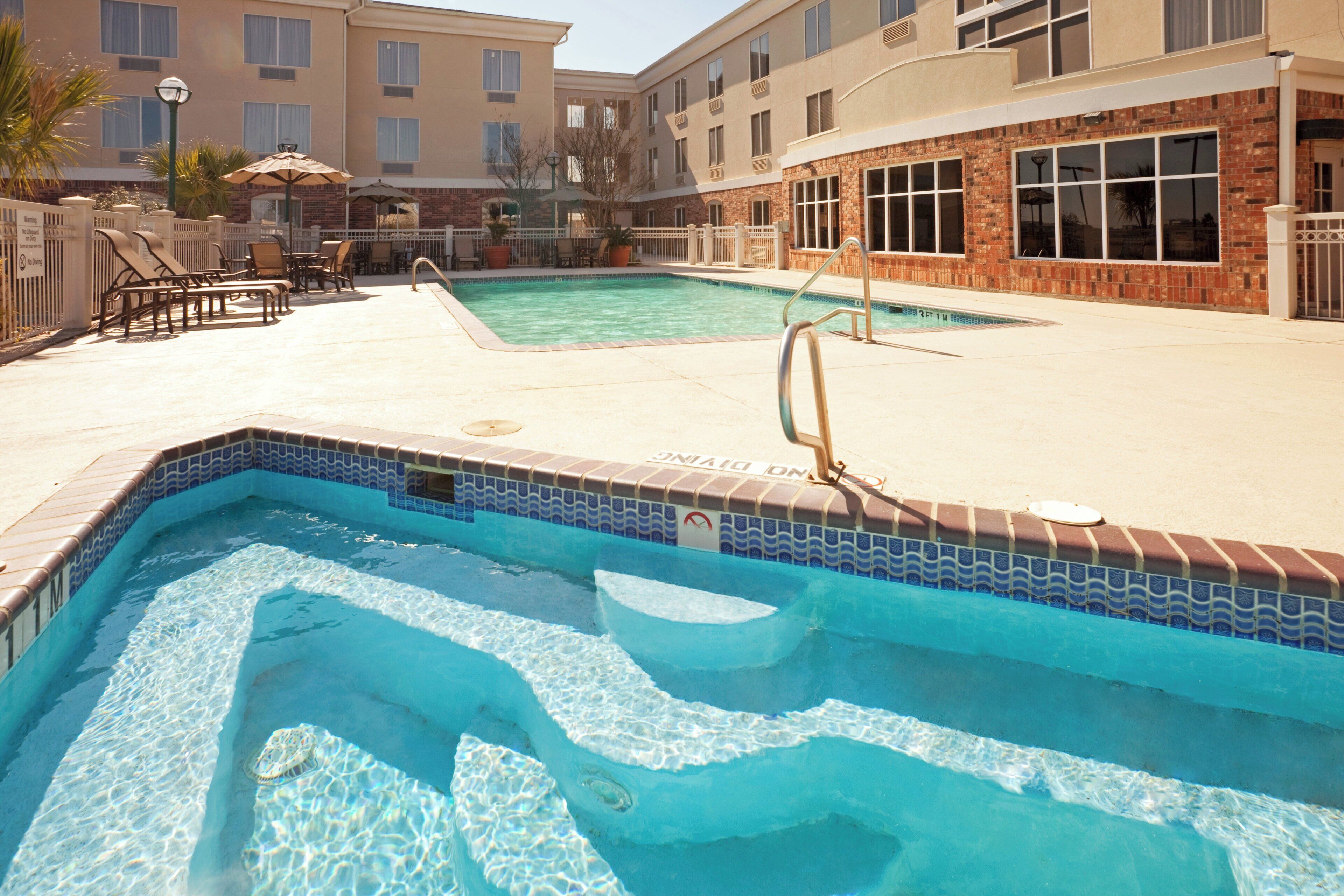 A swimming pool with a tiled edge, a diving board, and lounge chairs.