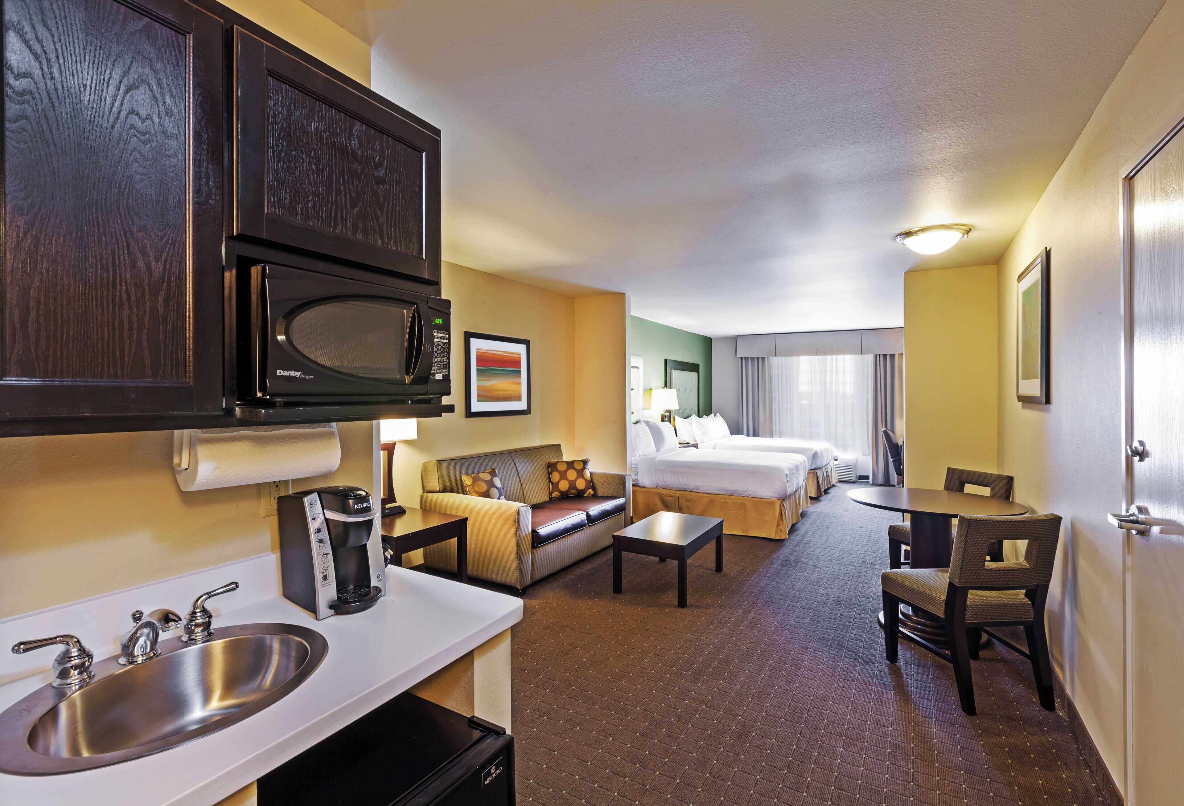 A hotel room with a kitchenette, a bed, a sofa, a dining table, and a bathroom.