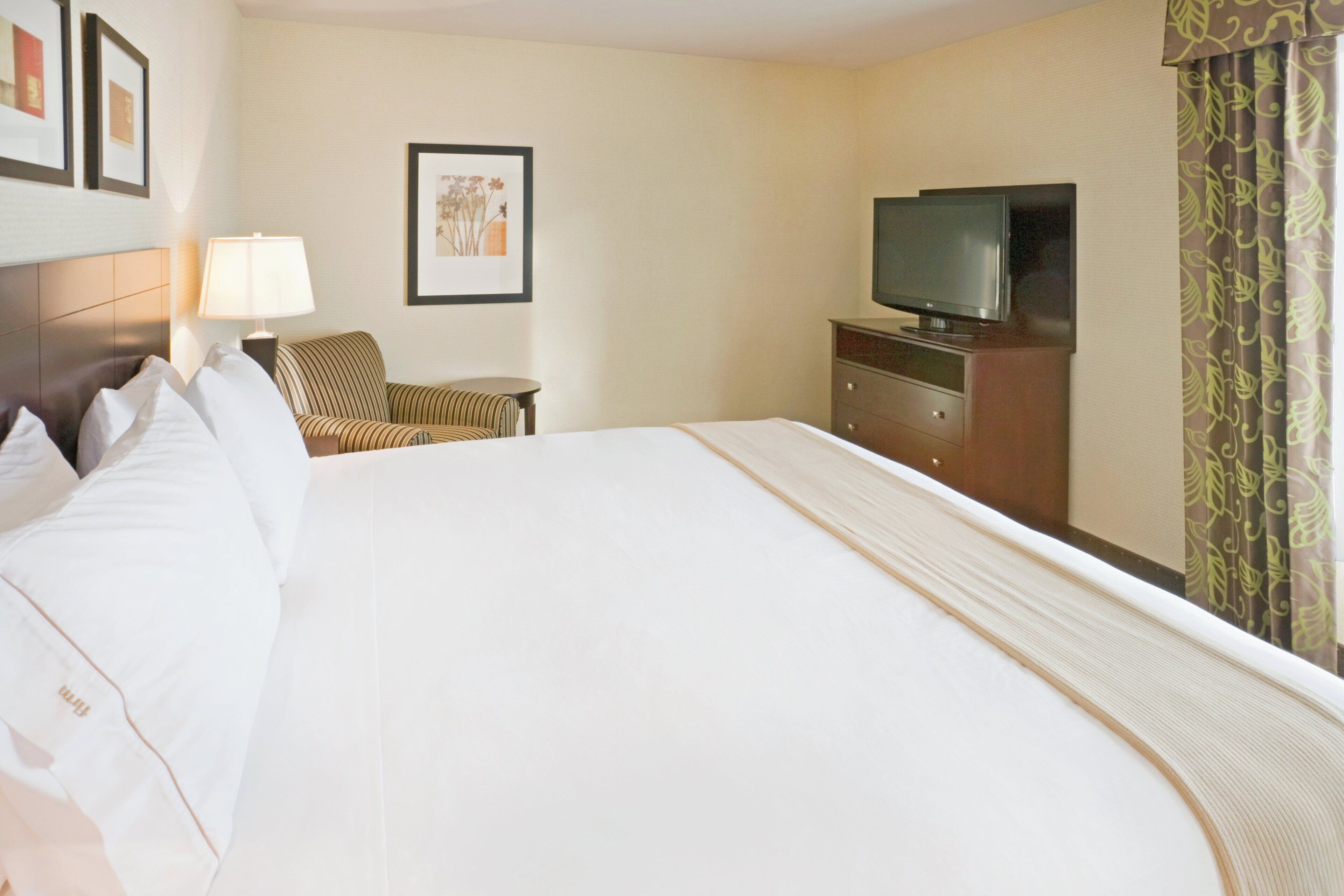Habitación de hotel con una cama grande, un televisor sobre una cómoda, una silla y una lámpara.